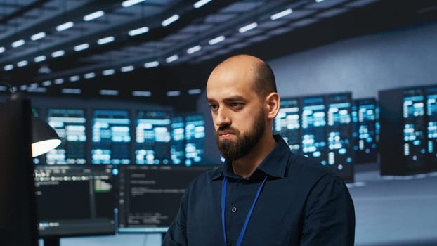 Computer scientist programming in data center room housing blade servers storing datasets. IT professional writing code on PC to mend data storage facility racks doing complex computational operations