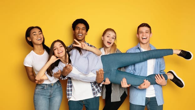 A diverse group of teenagers is seen gathering together and striking various poses in front of a camera, creating a lively and engaging atmosphere, holding their friend