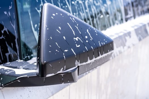 Denver, Colorado, USA-May 5, 2024-This image captures a close-up view of the Tesla Cybertruck side mirror covered in soap suds during a car wash, highlighting the vehicle distinctive angular design and rugged exterior.