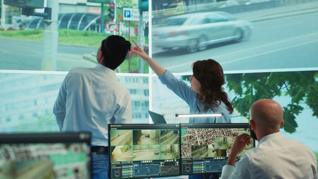 Diverse employees monitoring traffic via radar cameras at stop lights, using surveillance CCTV footage sensors in the city. People tracking cars in the government database, public safety. Camera A.