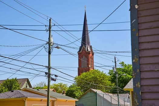 Historic church spire towers over Fort Wayne's vibrant, contrasting urban landscape and modern utilities.