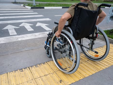 Rear view of an elderly woman in a wheelchair going to a pedestrian crossing. Close-up on wheels