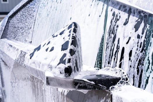 Denver, Colorado, USA-May 5, 2024-This image captures a close-up view of the Tesla Cybertruck side mirror covered in soap suds during a car wash, emphasizing the vehicle unique angular design and rugged exterior.