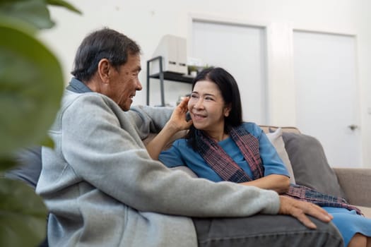 Older couples sit and chat and head over each other relaxed and happy on sofa at home on weekday in comfortable.