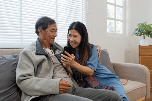 Happy married retirement couple looking at mobile using smartphone mobile technology device together, relaxing on couch doing online shopping.