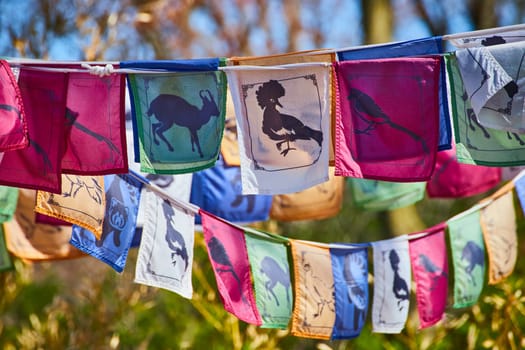 Colorful prayer flags with wildlife silhouettes flutter in a serene, natural setting at Fort Wayne, Indiana.