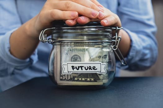 Female hands Saving Money In Glass Jar filled with Dollars banknotes. FUTURE transcription in front of jar. Managing personal finances extra income for future insecurity background