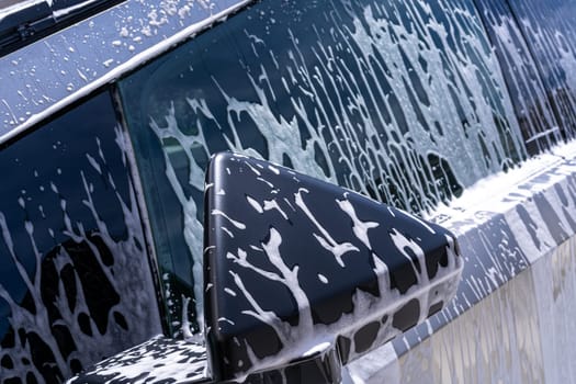Denver, Colorado, USA-May 5, 2024-This image captures a close-up view of the Tesla Cybertruck side mirror covered in soap suds during a car wash, emphasizing the vehicle unique angular design and rugged exterior.