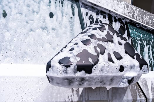 Denver, Colorado, USA-May 5, 2024-This image captures a close-up view of the Tesla Cybertruck side mirror covered in soap suds during a car wash, emphasizing the vehicle unique angular design and rugged exterior.