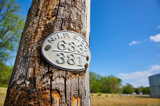 Aged wooden pole with historic plaque in rural Warsaw, Indiana, under a clear blue sky.