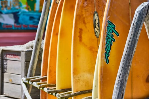 Colorful surfboards in a rack, sun-kissed and weathered, evoke vibrant beachside adventures.