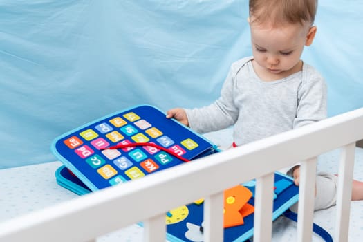 Little baby girl playing with busy book while sitting in crib. Concept of smart quiet books and modern educational toys