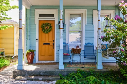 Charming light blue home in Fort Wayne with vibrant orange door and cozy porch, perfect for tranquil suburban living.