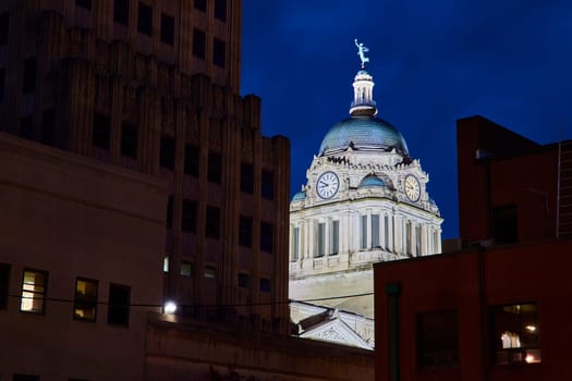 Illuminated Allen County Courthouse dome at blue hour, framed by modern silhouettes, Fort Wayne.
