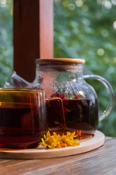 Calendula tea still life on table in green garden background. Healthy hot drink benefits. Natural organic aromatic drink in cup. Home-grown immunity-boosting herbs for tea. Autumn winter warming calming drink