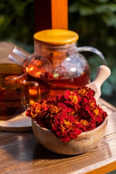 Marigold flower healthy tea in glass mug with tea pot on garden table. Herbal medicine Delicious tisane tea with fresh yellow blossom dandelion flowers tea cup. Green clearing infusion Wildflowers Eco friendly sustainable eating