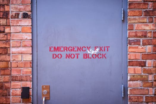 Weathered emergency exit door on a brick wall, Fort Wayne, highlighting safety and urban decay.