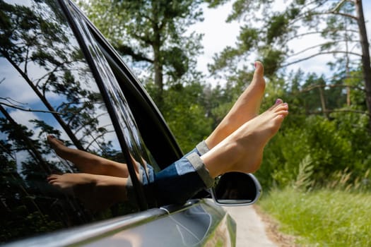 Female legs in blue jeans out of car window. Concept of comfortable local travel vacation holiday. Reduce carbon footprint. Woman resting in road trip refresh and recharge