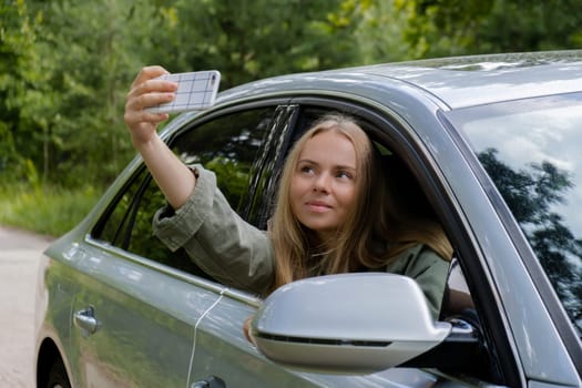 Blonde woman stoped car on road to take a selfie photo. Young tourist explore local travel making candid real moments. True emotions expressions of getting away and refresh relax on open clean air