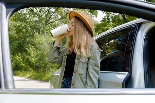 Smiling young woman drinking coffee or tea from reusable thermos cup. Traveler making a coffee break in Local solo travel on weekends concept. Exited woman explore freedom outdoors in forest. Unity with nature lifestyle, rest recharge relaxation