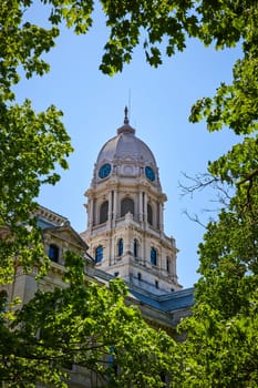 Historic Kosciusko County Courthouse, Indiana, framed by lush foliage under a clear blue sky.