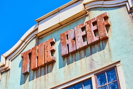 Vintage 'THE REEF' sign on a rustic sea green wall, showcasing historical decay under bright daylight.