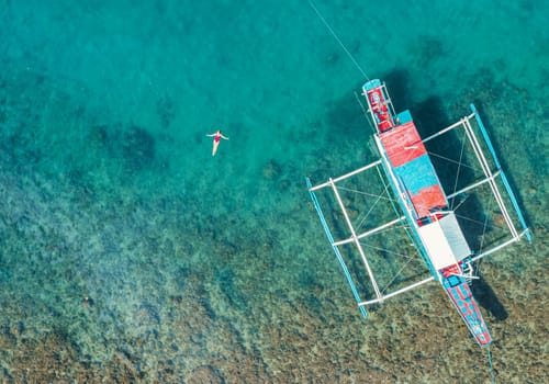 Aerial View of a Woman in Red Swimsuit Floating Serenely on the Crystal Clear Ocean Waters During Midday