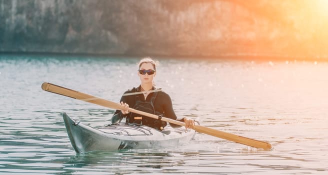 Happy smiling woman in kayak on ocean, paddling with wooden oar. Calm sea water and horizon in background