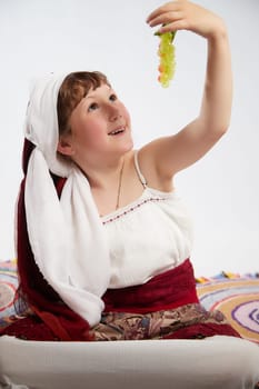 Portrait of Little girl in a stylized Tatar national costume with berries and a brush of grapes on a white background in the studio. Photo shoot of funny young teenager who is not a professional model
