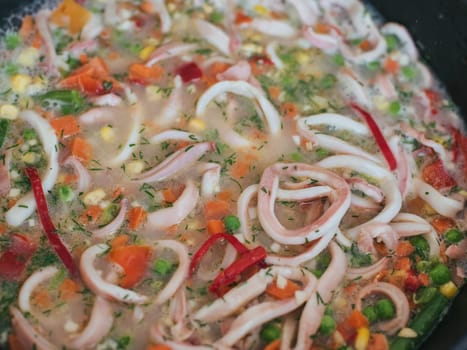 Squid rings with vegetables stewed in a frying pan close-up