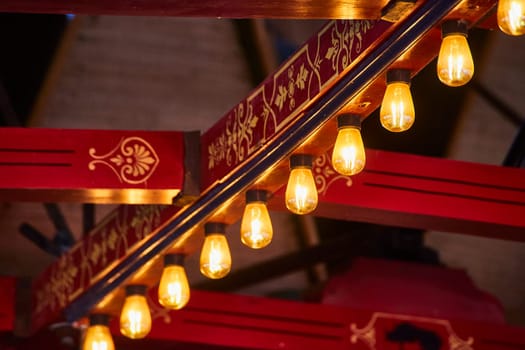 Warm Edison bulbs glow beneath a rich, red and gold railing, blending tradition with modernity in an intimate setting.