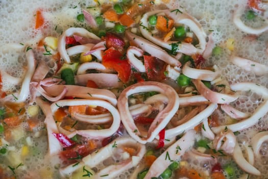 Squid rings with vegetables stewed in a frying pan close-up
