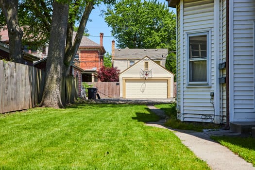 Sunny suburban backyard in Fort Wayne with lush lawn, large tree, and basketball hoop.