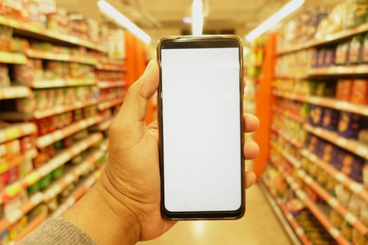 hand holding mobile phone with white screen while shopping at supermarket