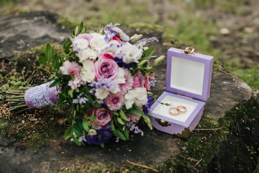 wedding rings in a box next to the bouquet lie on the stump