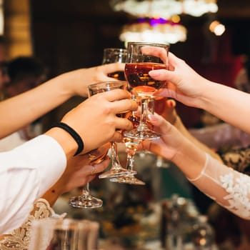 hands of a group of people clinking and toasting glasses of red wine at a festive party in a restaurant. Concept of friendship and success