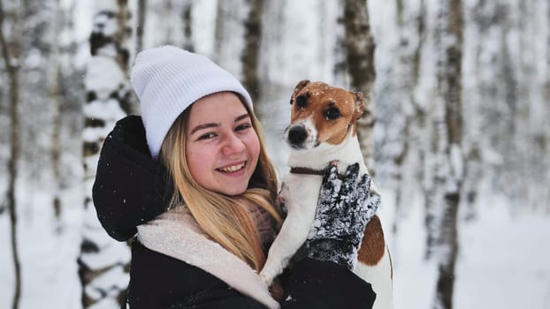 A girl cuddles a Jack Russell Terrier dog in the woods in winter