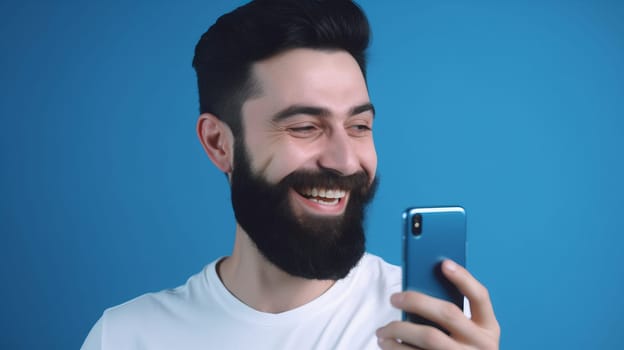 A happy man-a brunette with a beard, in a white shirt, standing isolated on a blue background, holding a smartphone in his hands. close up. Copy space