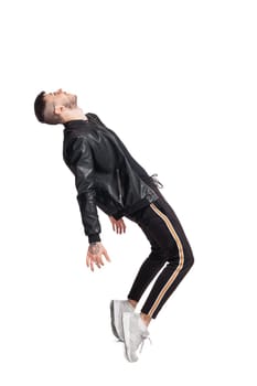 Full-length photo of a modern performer in glasses, black leather jacket, t-shirt, sports pants and light sneakers fooling around tilting back in studio. Indoor photo of a funny fellow dancing isolated on white background. Music and imagination.