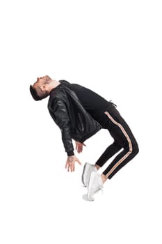 Full-length photo of a modern performer in glasses, black leather jacket, t-shirt, sports pants and light sneakers fooling around tilting back in studio. Indoor photo of a funny guy dancing isolated on white background. Music and imagination.