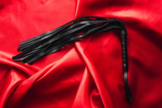 leather black whip for sex games in bdsm sex on red silk background