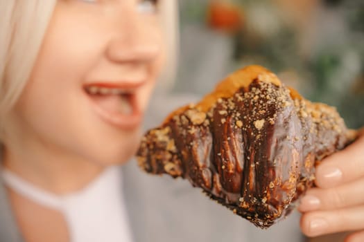 A blonde woman is eating a chocolate covered pastry. She is smiling and she is enjoying her treat