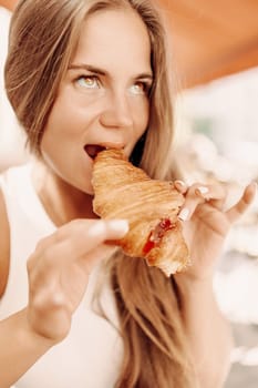 A woman is eating a croissant. The croissant is half eaten and has a jelly filling