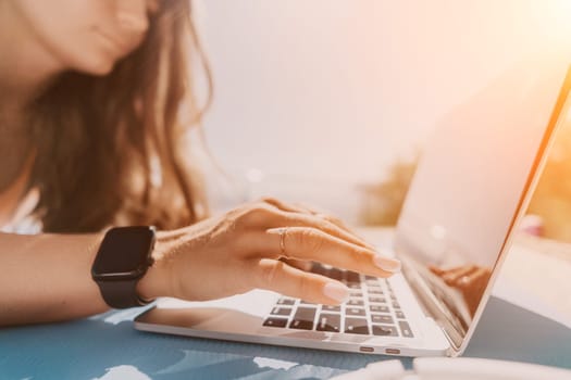 Digital nomad, Business woman working on laptop by the sea. Pretty lady typing on computer by the sea at sunset, makes a business transaction online from a distance. Freelance, remote work on vacation