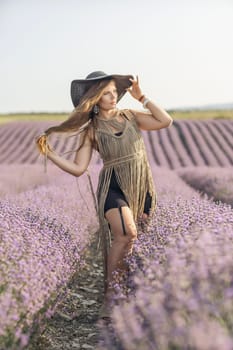 A woman is standing in a field of purple flowers, wearing a black dress and a black hat