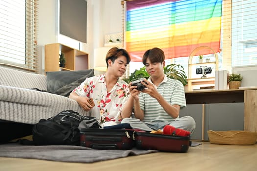 Homosexual couple packing travel bag for summer vacation in living room.