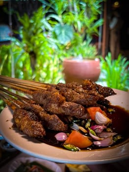 Lamb, mutton grilled skewer satay served with soy sauce sauce with sliced shallots, tomatoes, cucumber and cayenne pepper served in white plate