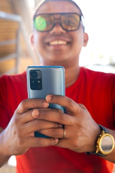 Happy Latin man smiling while browsing the internet with a telephone feeling of happiness looking at camera outdoors.