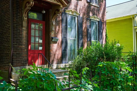 Charming vintage brick home with a striking red door, nestled in a lush Fort Wayne neighborhood.