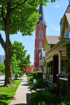 Tranquil suburban street in Fort Wayne, with historic homes and a striking red brick church, under a clear blue sky.